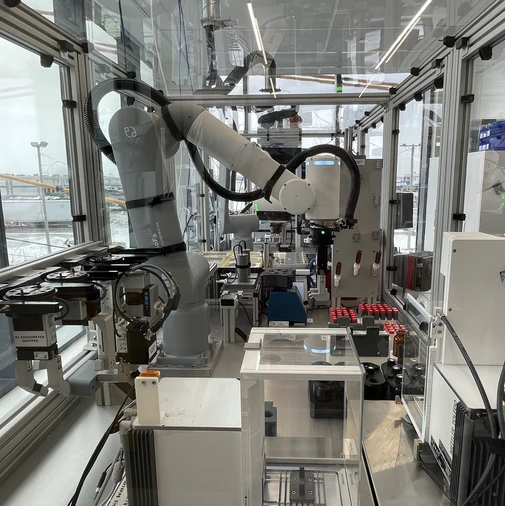 Robotic arm within an encasement, insert chemicals into vials, showcasing a real world example of Atinary's Self Driving Labs in action.