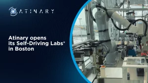 A promotional graphic for Atinary Technologies featuring a robotic arm operating in a laboratory setting, with the text "Atinary Opens its Self-Driving Labs® in Boston."