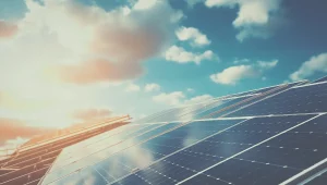 An array of solar panels angled toward a bright, sunlit sky with scattered clouds at sunset.